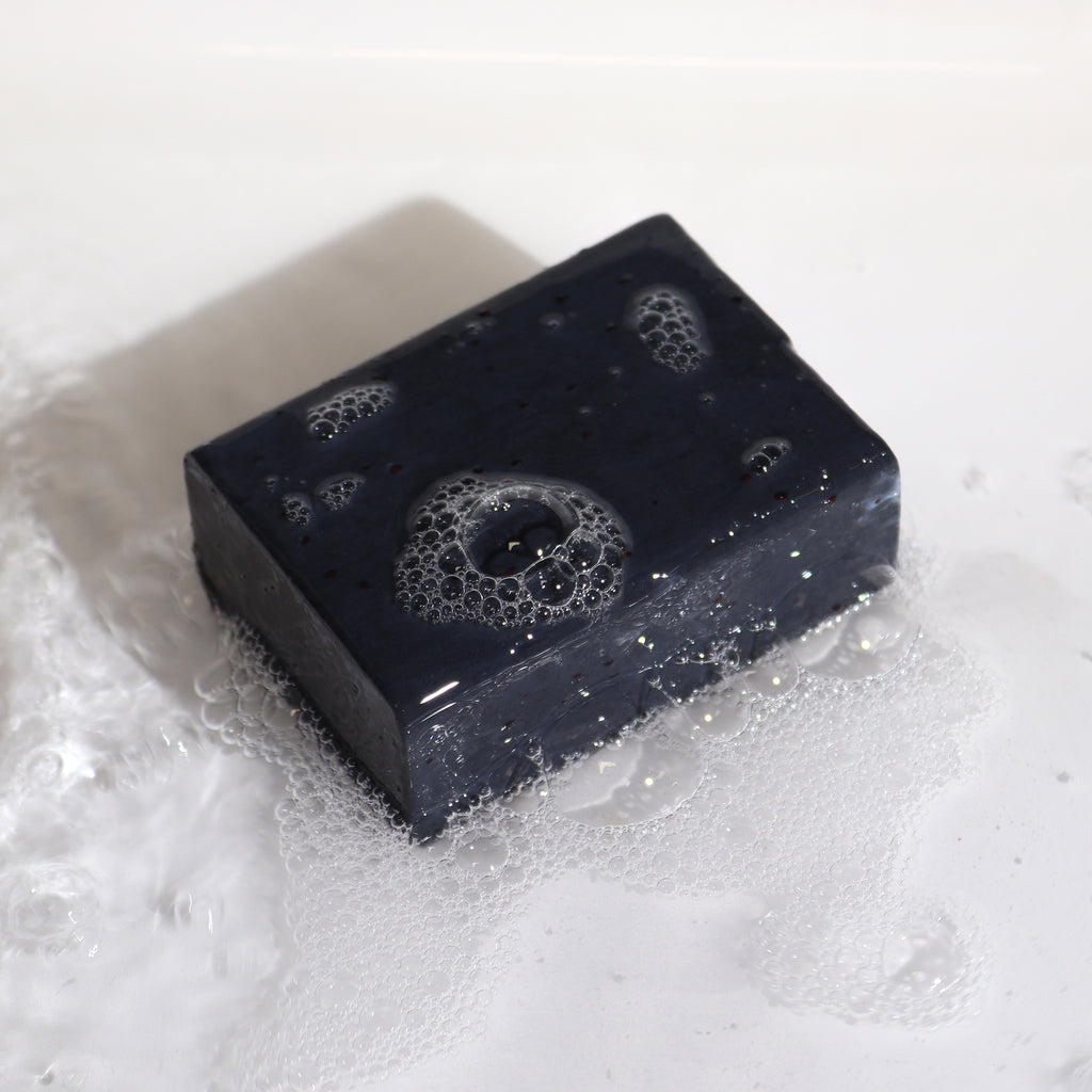 Klay Soap - Bergamot & Sandalwood. A rectangular bar of natural, dark-coloured soap with visible cranberry seeds for exfoliation. The soap is infused with Fuller's earth clay and activated charcoal for detoxifying properties.